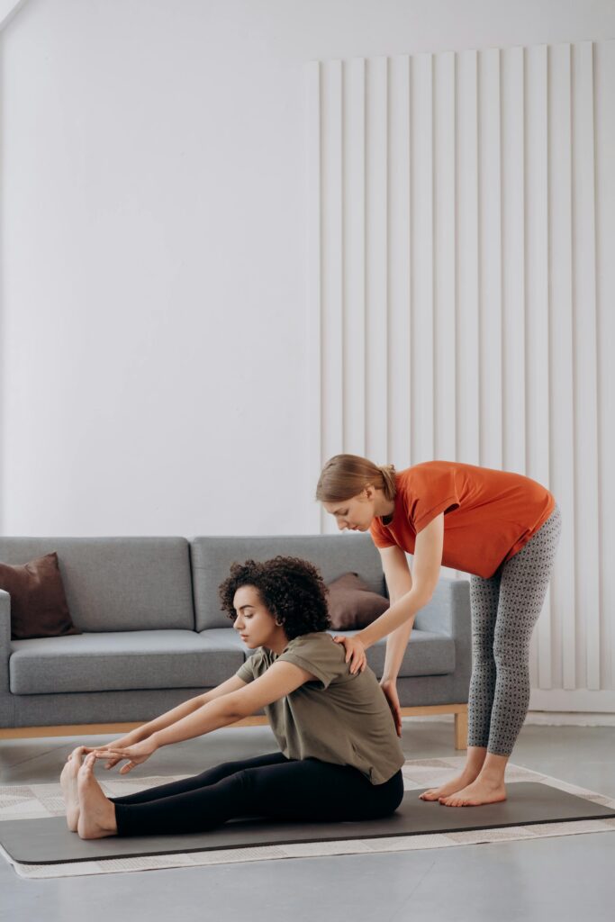 Two women engaging in a yoga session indoors, focusing on flexibility and wellbeing.